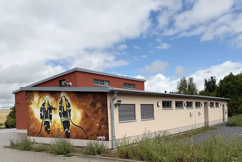 Blick auf das verputzte Feuerwehrgerätehaus mit Wandmalerie